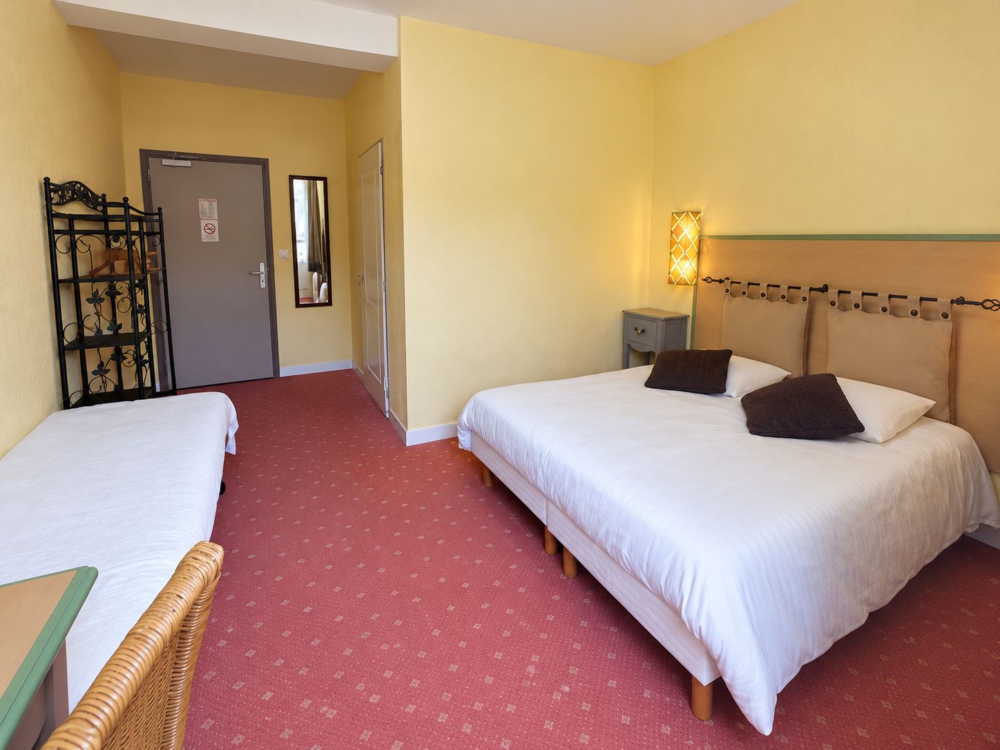 Habitación de hotel con dos camas, alfombra roja, cabecero de madera, mesita de noche y lámpara de pared.