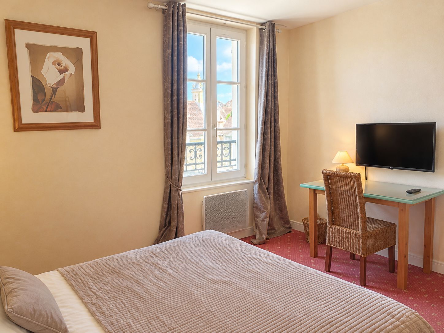 A hotel room with a bed, a desk with a chair, a television, and a window with curtains.