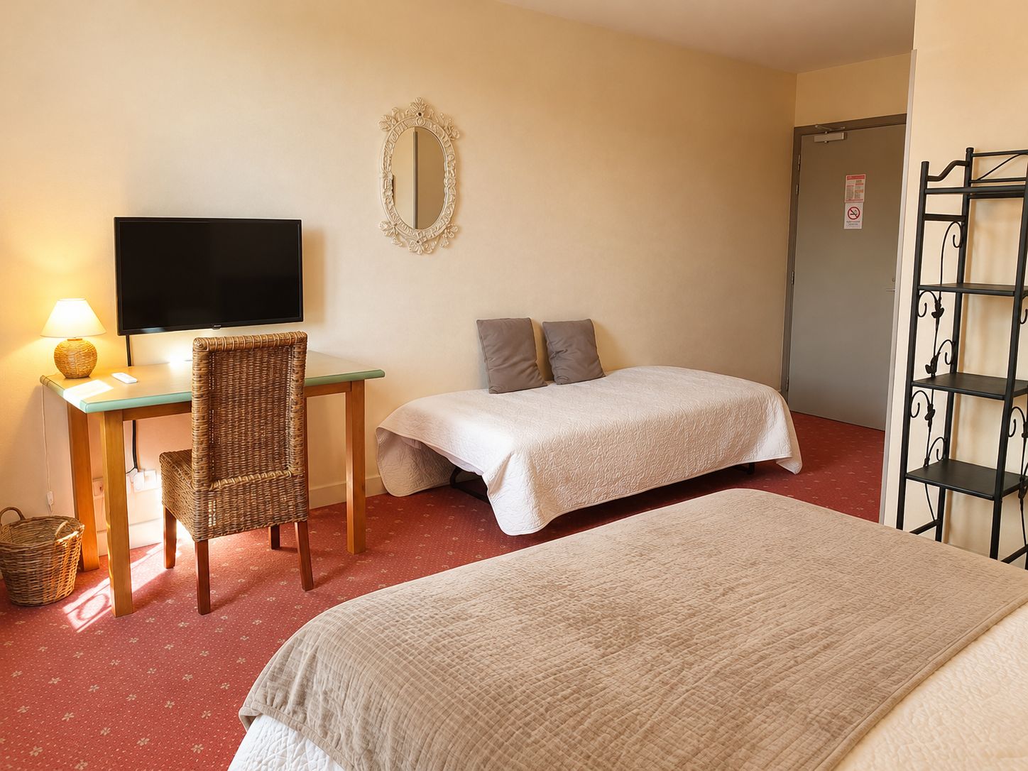 Habitación de hotel con dos camas, un escritorio con televisor, una silla, un espejo y una estantería.