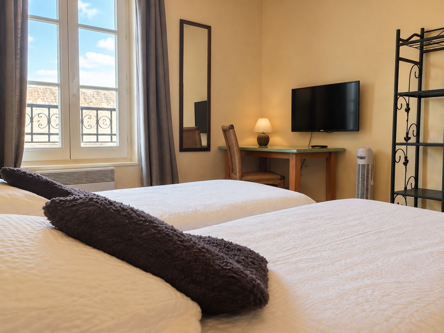 A hotel room with two beds, a desk with a lamp, a TV, and a window with curtains.