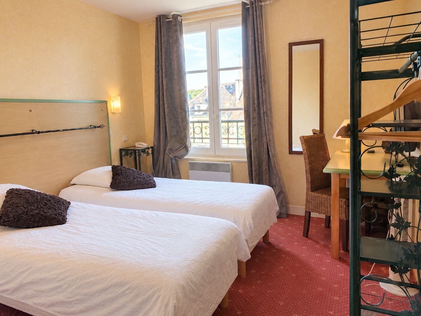 Une chambre d’hôtel avec deux lits, un bureau, une chaise et une fenêtre avec des rideaux.