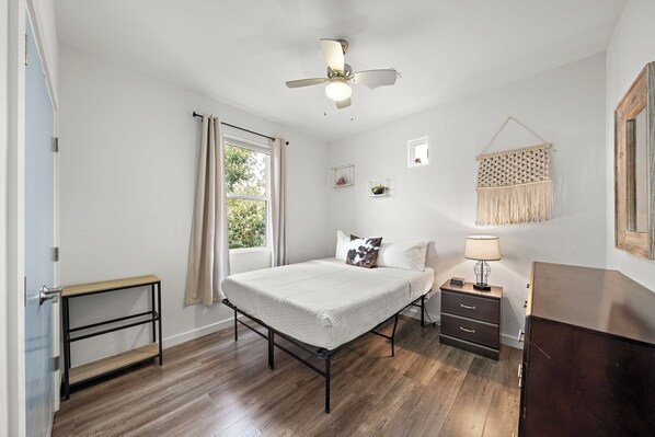 A bedroom with a bed, bedside table, lamp, and a ceiling fan.