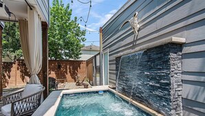 Una piscina con una cascada de piedra, rodeada por una terraza de madera y una silla de mimbre.
