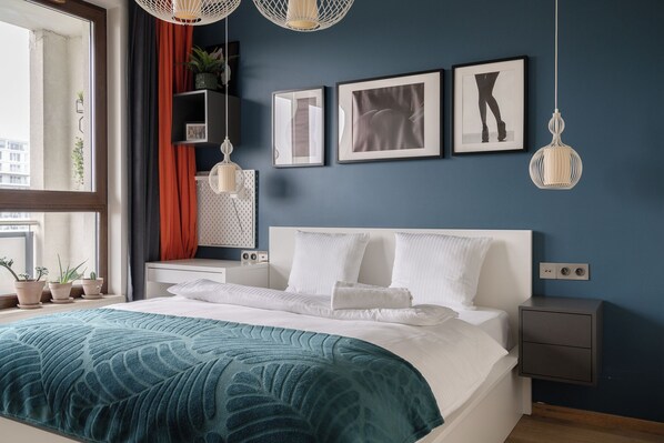Une chambre à coucher moderne avec un grand lit, une table de chevet, une commode et une fenêtre avec des rideaux.
