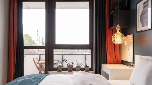 Een hotelkamer met een bed, nachtkastje en een raam met gordijnen.