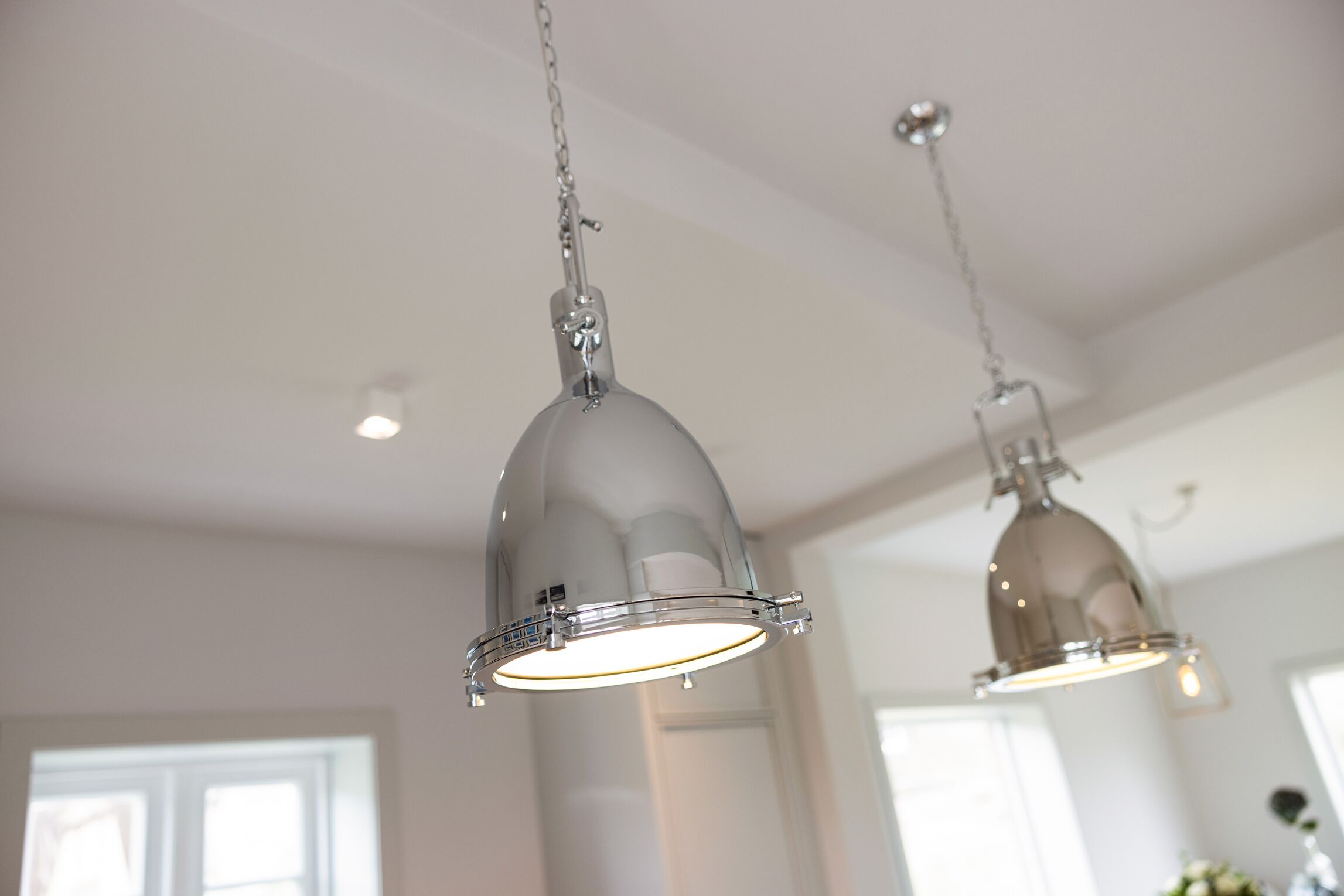 Two pendant lights hanging from the ceiling in a room with white walls and a window.