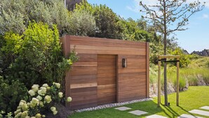 A modern wooden structure with a door, surrounded by lush greenery and a well-maintained lawn. - Heide.Way - List on Sylt (List auf Sylt)