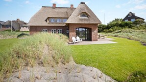 A house with a thatched roof, brick walls, and a large glass door entrance. - Heide.Way - List on Sylt (List auf Sylt)