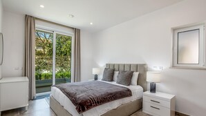 A modern bedroom with a large bed, a nightstand, a bedside table, and a view of greenery through the window. - Villa Praia de Branson, with amazing Ocean views (Lagos)