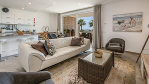 A modern living room with a sofa, a coffee table, and a chair. There is a kitchen area with cabinets and a dining table. - Villa Praia de Branson, with amazing Ocean views (Lagos)