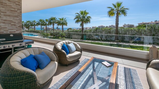 A balcony with wicker furniture, a grill, and a view of palm trees and buildings. - Villa Praia de Branson, with amazing Ocean views (Lagos)