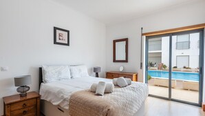 Une chambre à coucher avec un lit, des tables de chevet, un miroir et une vue sur une piscine.