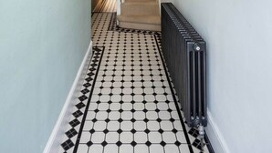 Un couloir doté d’un sol à motifs géométriques, d’un radiateur, d’une étagère en bois avec un miroir et d’un escalier menant à une autre pièce.