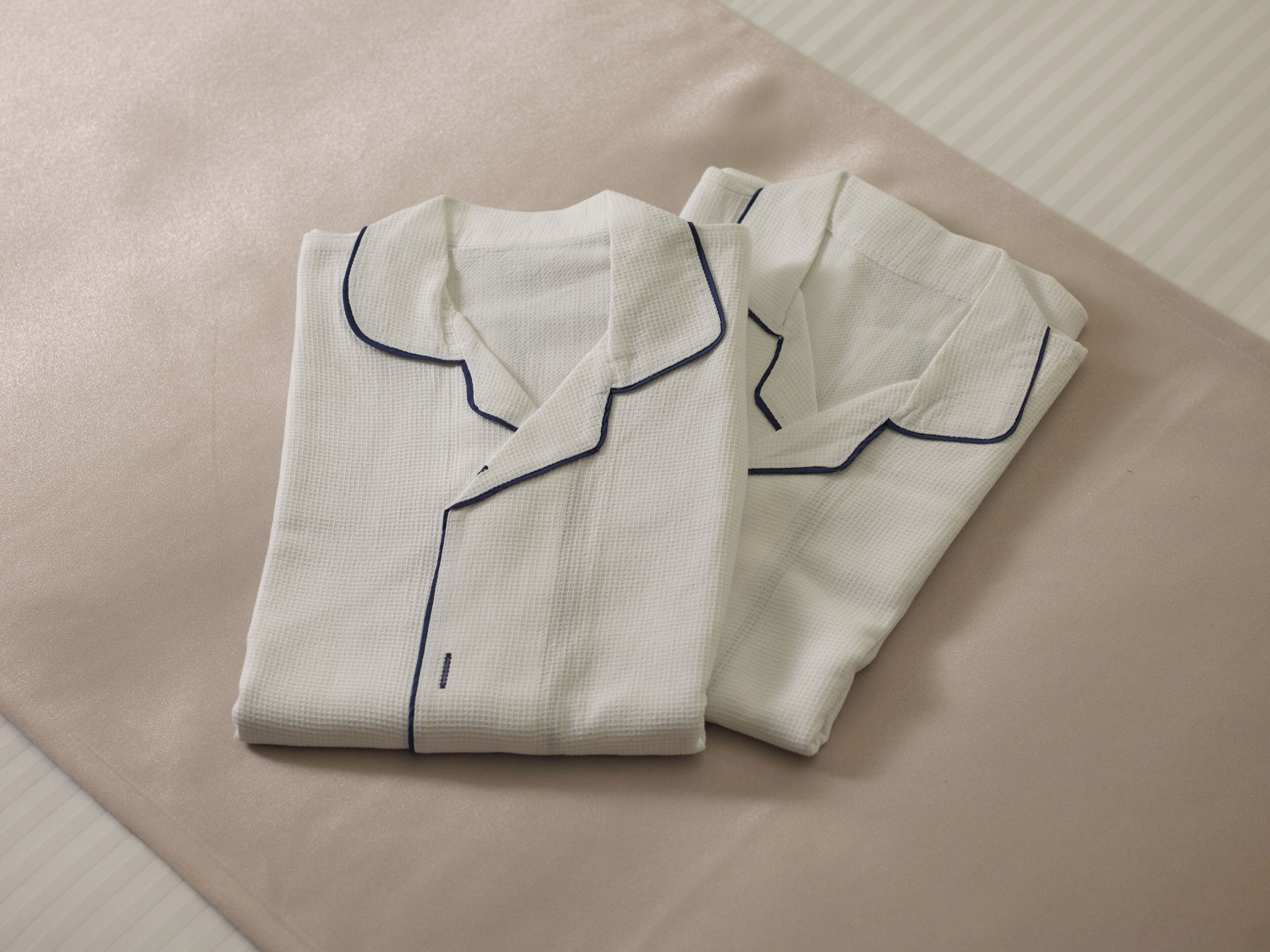 Neatly folded white shirts with dark blue piping on a textured beige surface.