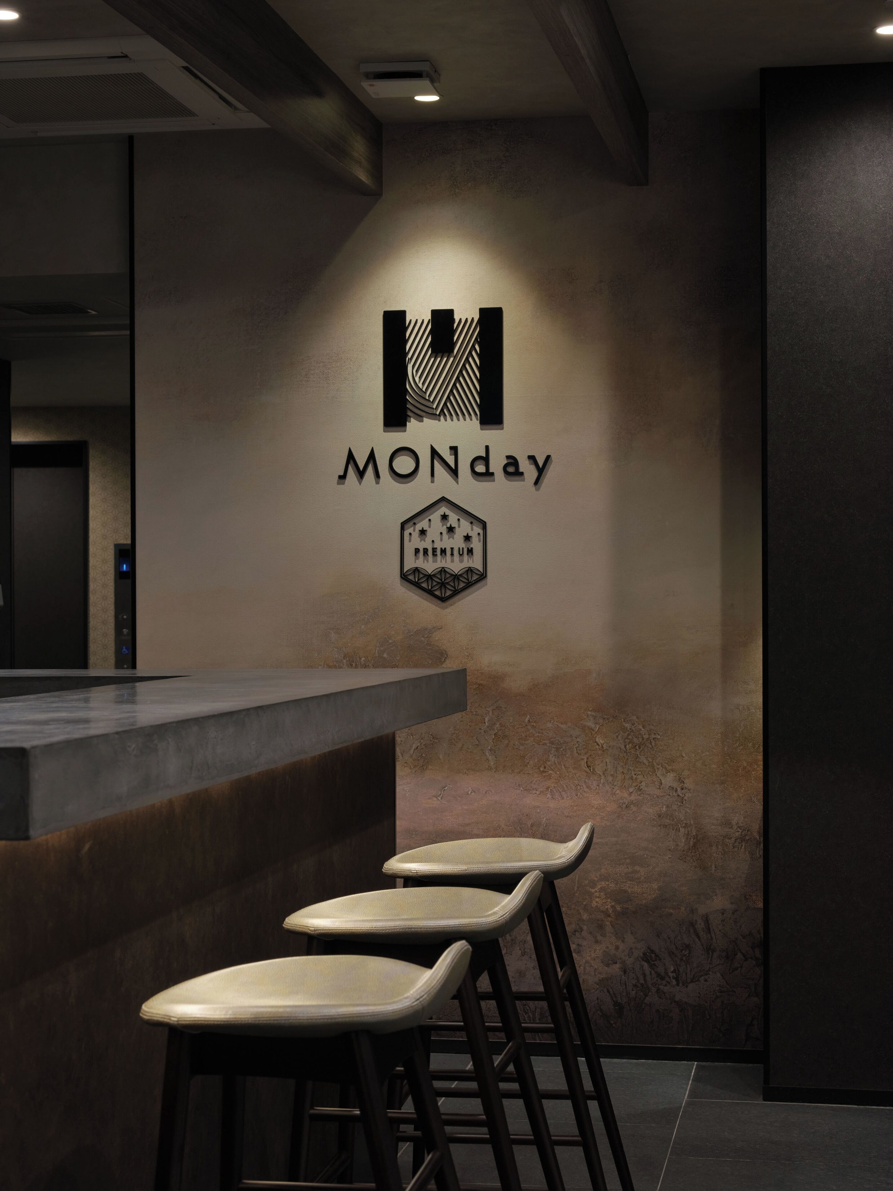 Eine Bar mit Sitzhocker und einem an der Wand befestigten Logo mit der Aufschrift 'MONDAY PREMIUM'.