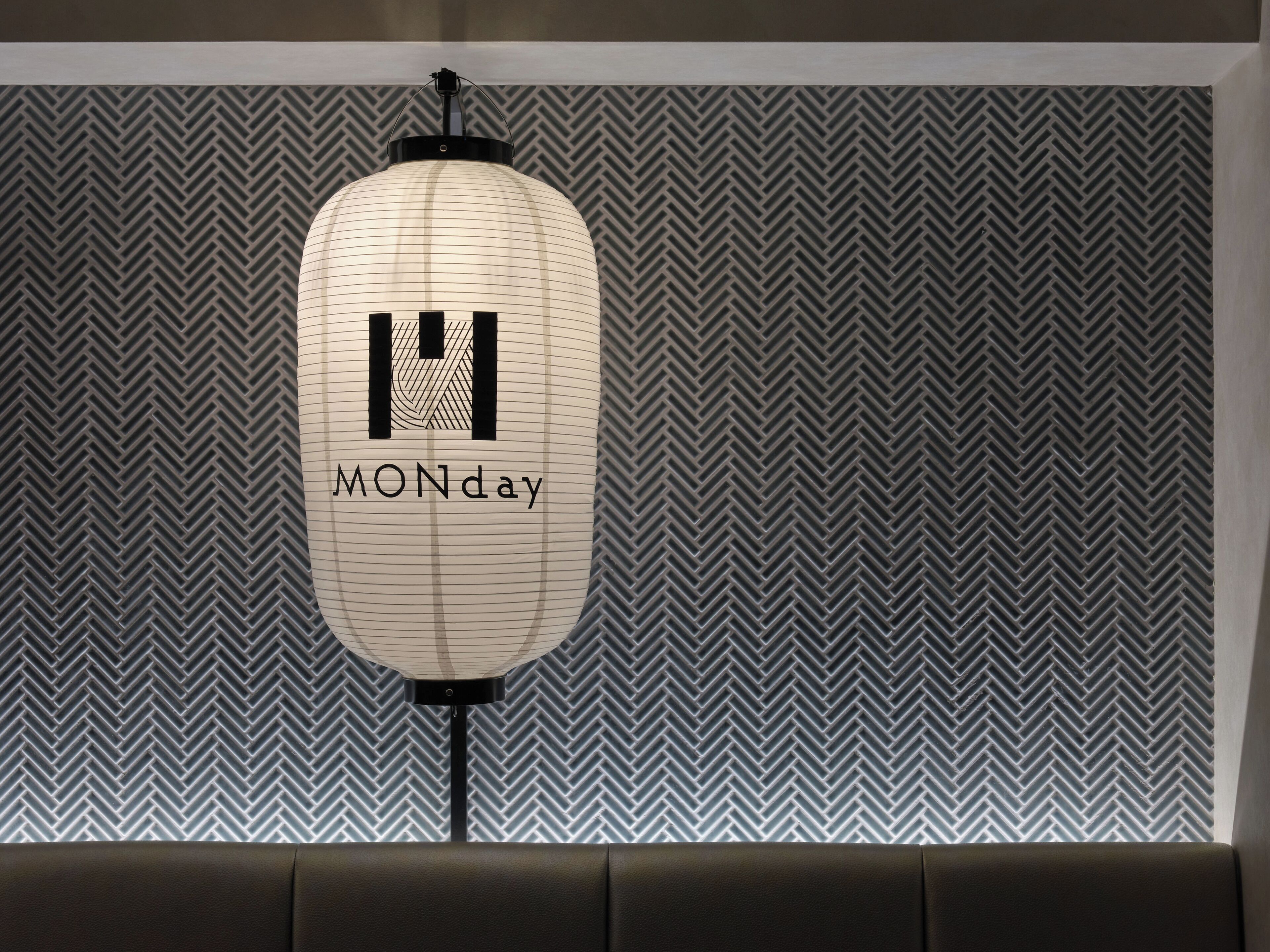 A wall with a herringbone pattern and a hanging light fixture with a geometric design.