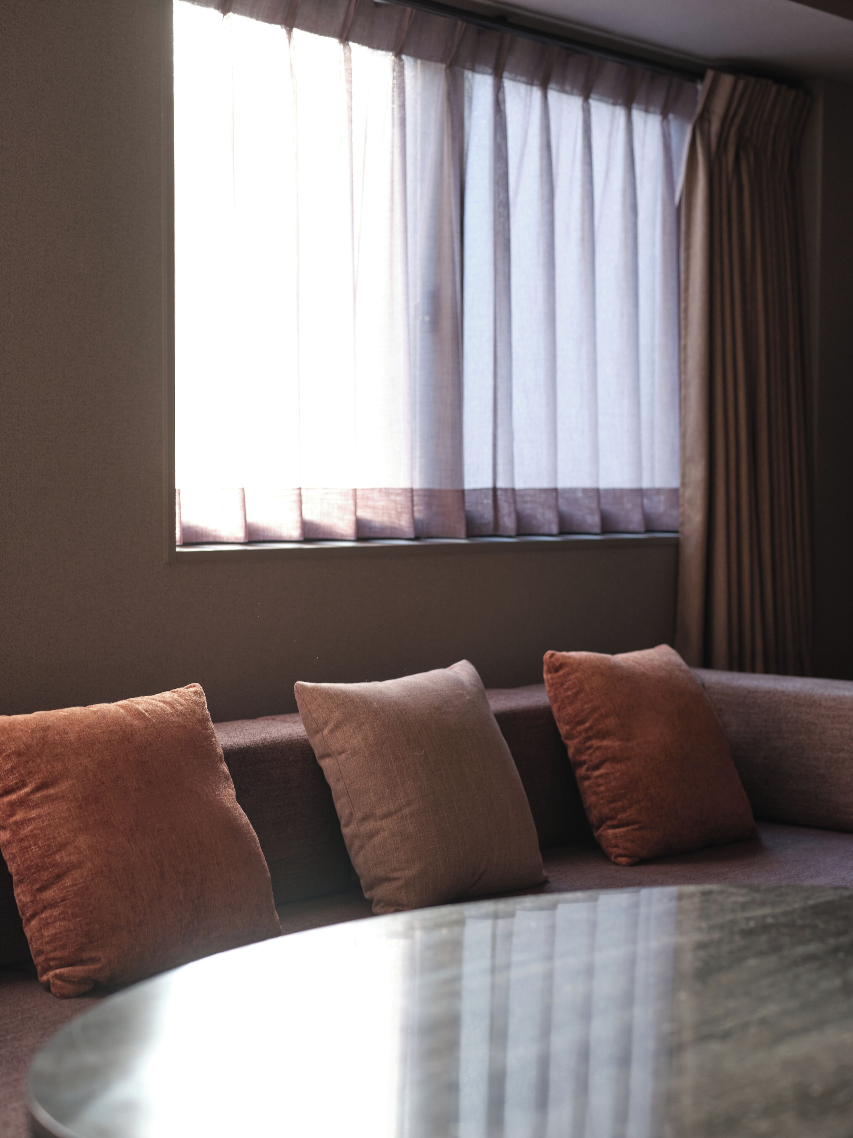 Ein Zimmer mit einem runden Tisch, einer Couch mit Kissen und einem Fenster mit Vorhängen.