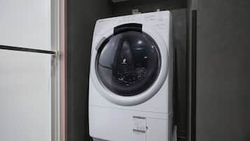 A compact, modern washing machine in a small laundry room with a wooden floor and a white door.