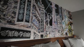 Quarto de hotel com uma grande pintura abstrata na parede, cabeceira de madeira e roupa de cama branca.