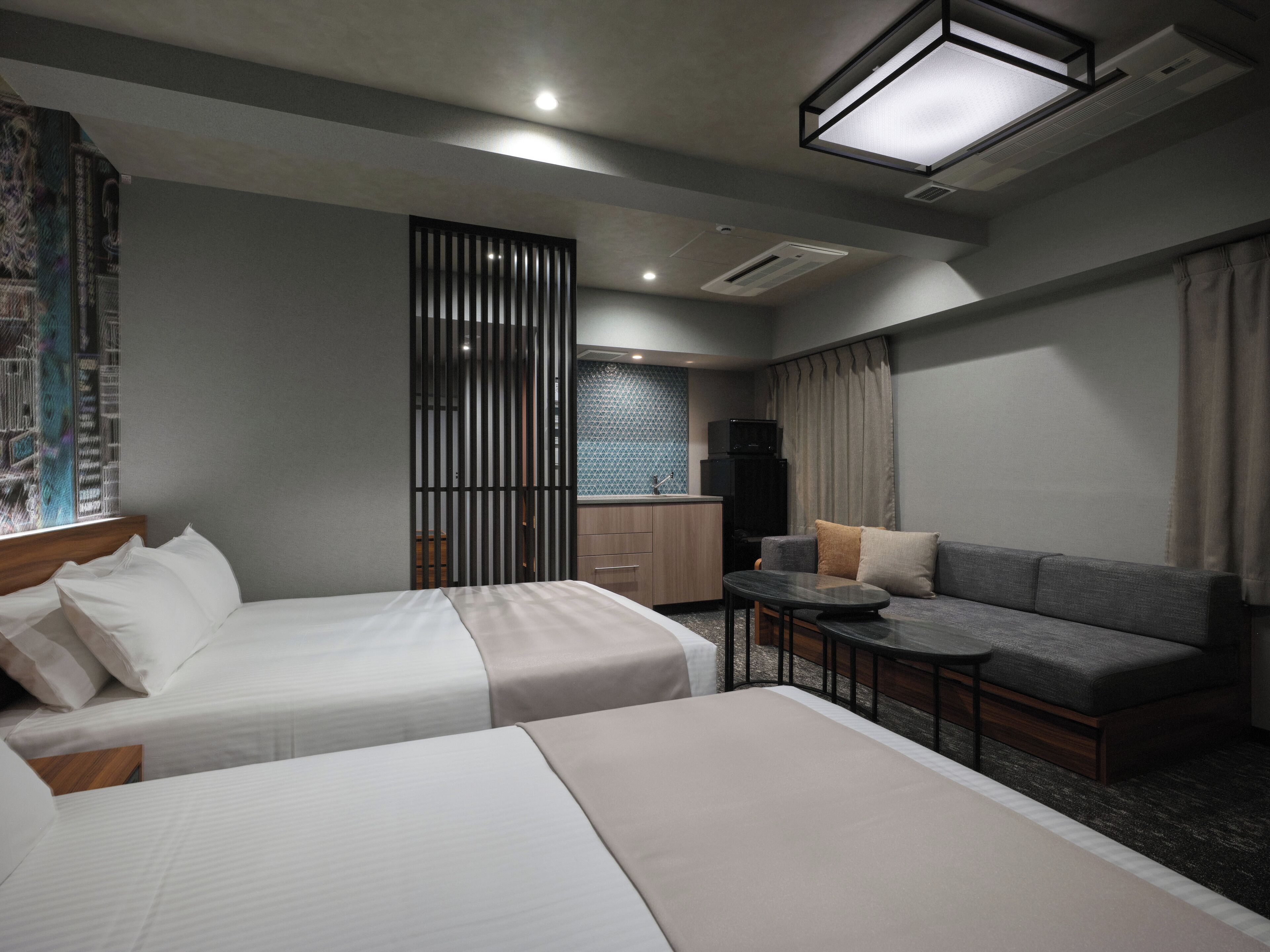 Habitación de hotel con dos camas, un sofá, una pequeña mesa y una kitchenette.