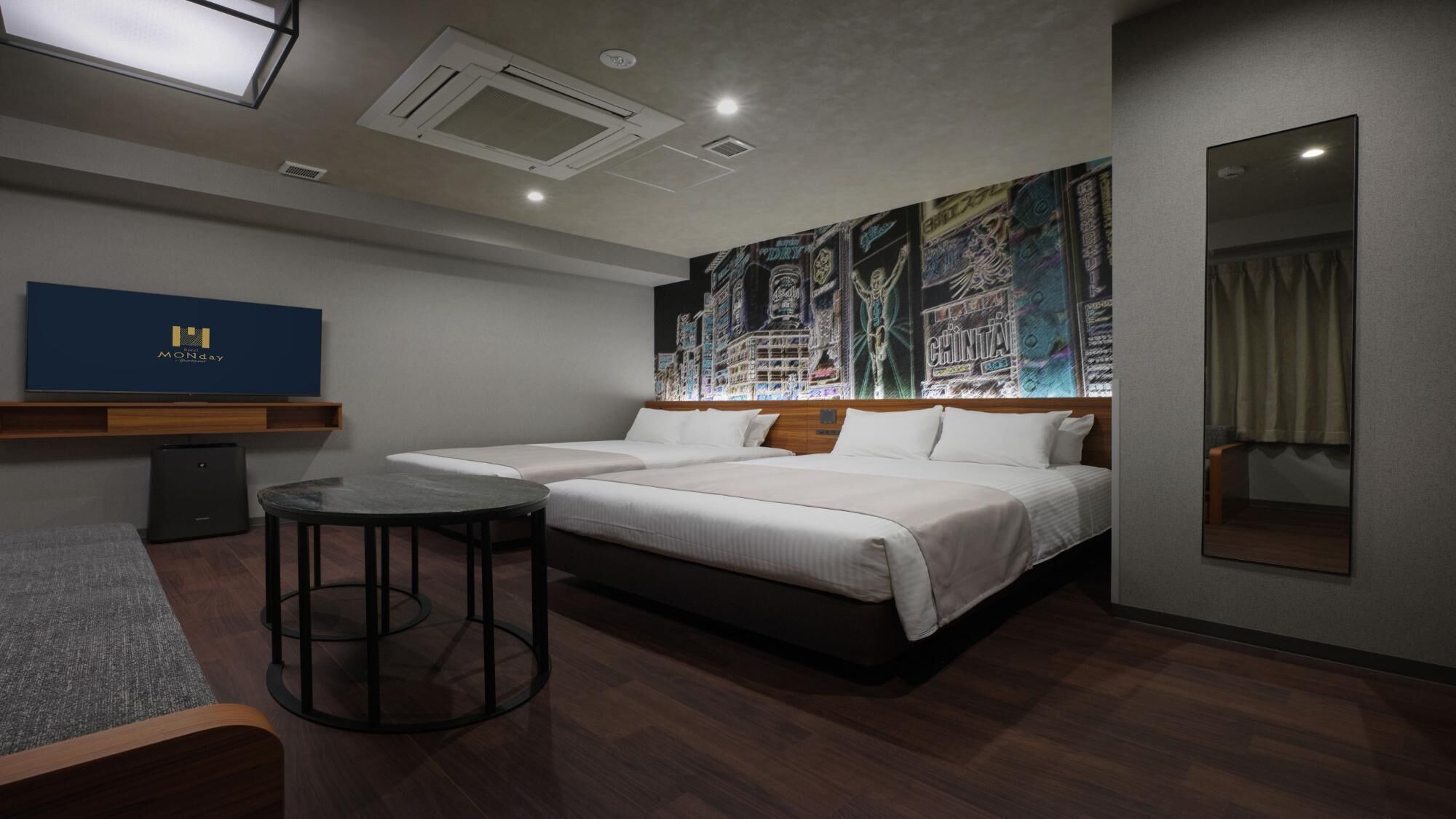 A hotel room with a bed, a small round table, a mirror, a wall-mounted TV, and a ceiling light.