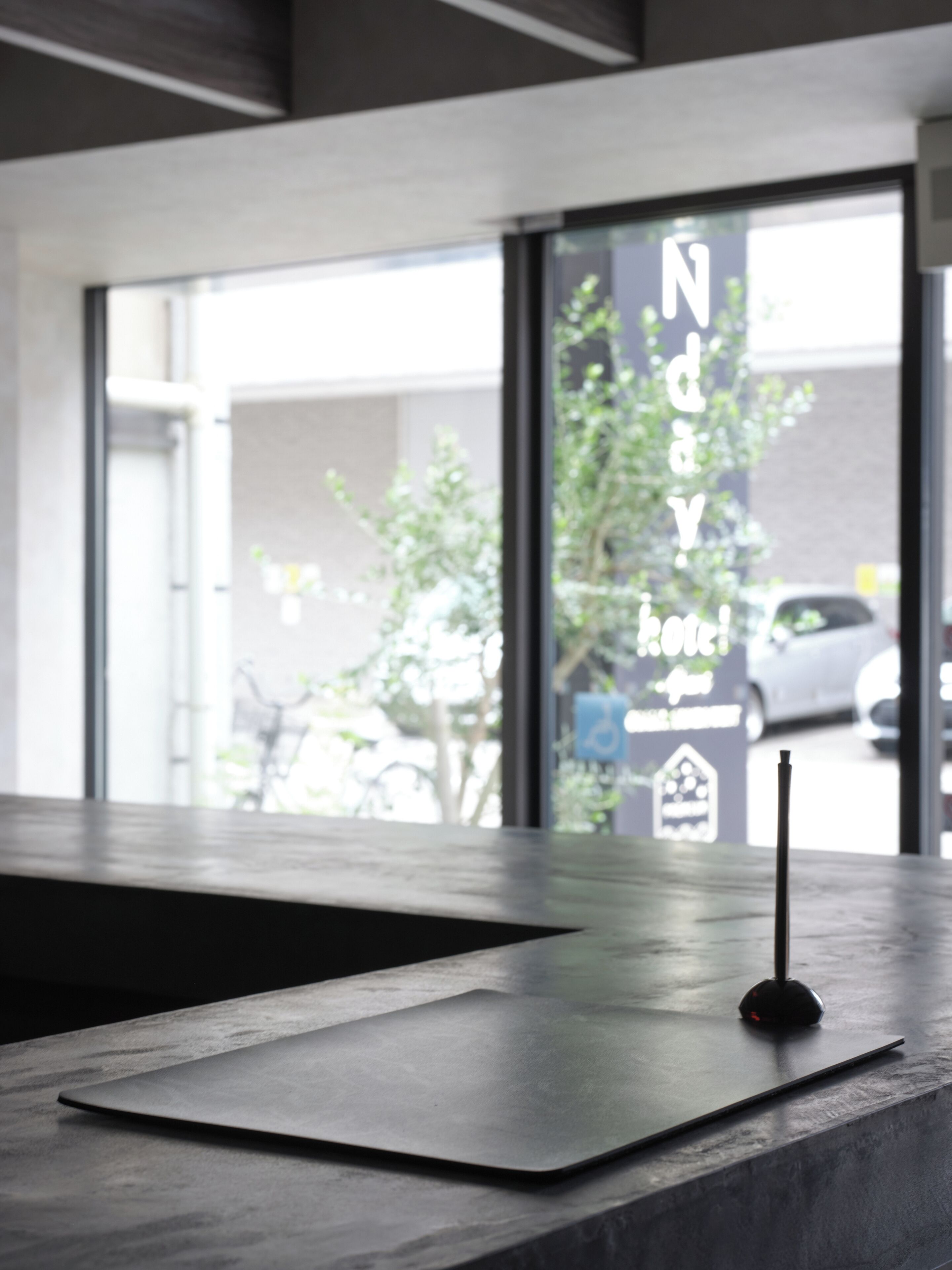Un hall d’accueil d’hôtel moderne, au design minimaliste, comprenant un comptoir d’accueil et une grande fenêtre donnant sur la rue et les voitures garées à l’extérieur.