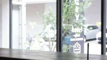 Un hall d’accueil d’hôtel moderne, au design minimaliste, comprenant un comptoir d’accueil et une grande fenêtre donnant sur la rue et les voitures garées à l’extérieur.