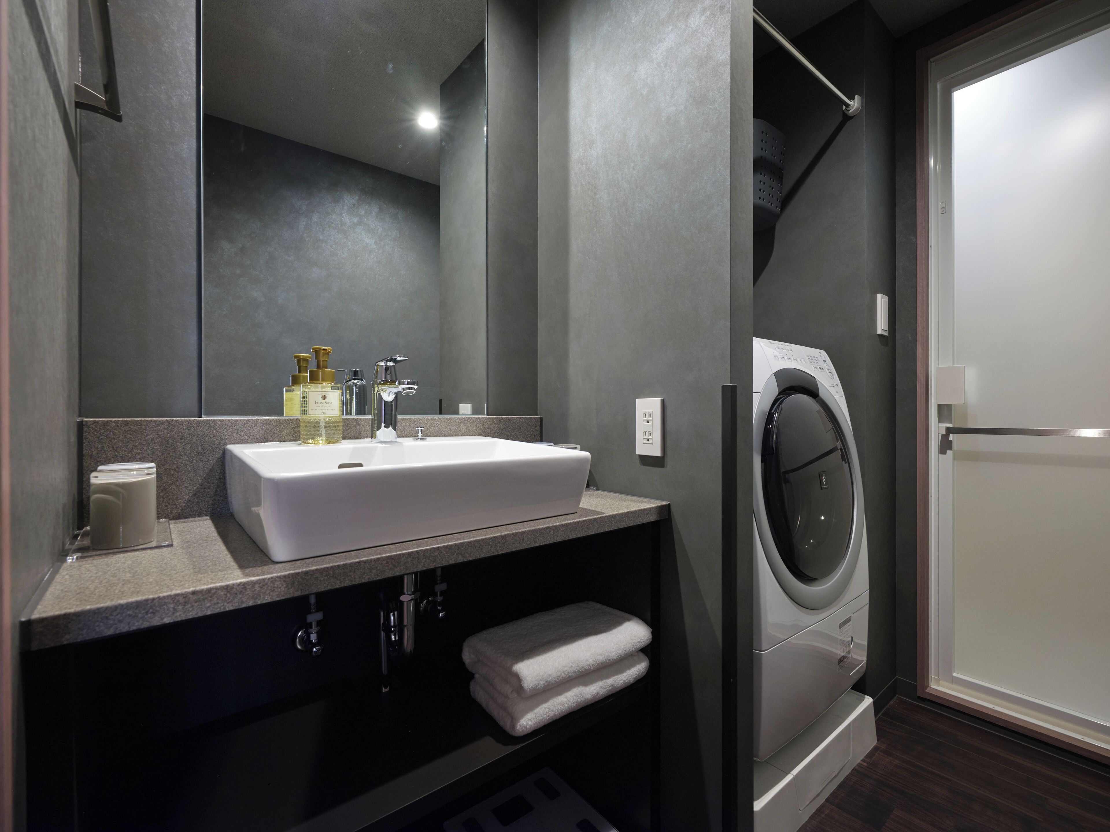 A modern bathroom with a large sink, mirror, and a built-in washing machine.