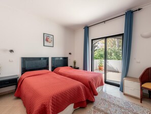 A bedroom with two beds, a large sliding glass door, a small wooden chair, and a potted plant. - Apt. Alto Golf E2A, with access to a communal pool (Alvor)