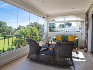 Un balcó amb moble de vugada, un sofà verd amb coixinets grocs, i vista sobre un camp de golf i edificis.