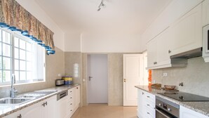 A kitchen with white cabinets, a stainless steel sink, a built-in oven, and a window with a curtain. - Casa Oliveiras, villa with private pool & garden (Alvor)