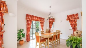 A dining area with a wooden table and chairs, red patterned curtains, a potted plant, and a hanging light fixture. - Casa Oliveiras, villa with private pool & garden (Alvor)
