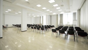 A large conference room with rows of chairs, a projector screen, and a large window with curtains. - Sunrise Hotel (Casoria)