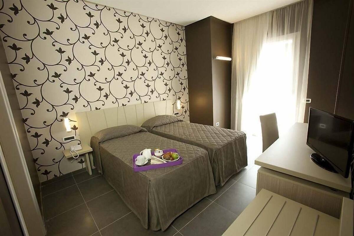 Hotellihuone, jossa on kaksi sänkyä, televisio ja aamiaistarjoilu vasemmanpuoleisella sängyllä.
