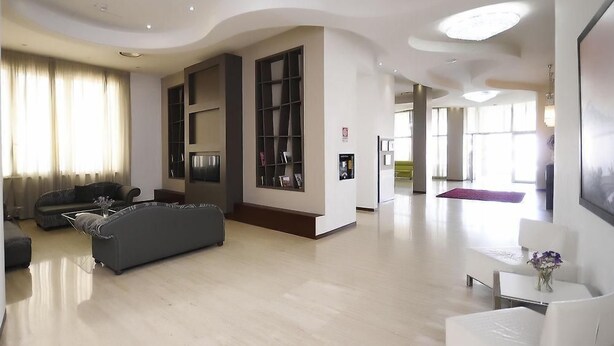 A spacious living room with a grey sofa, a coffee table, and a bookshelf. - Sunrise Hotel (Casoria)
