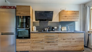A modern kitchen with wooden cabinetry, a built-in oven, and a stainless steel refrigerator. - Charming 2-room in Val d'Isère - WIFI, for 4 pers (Val-d'Isère)