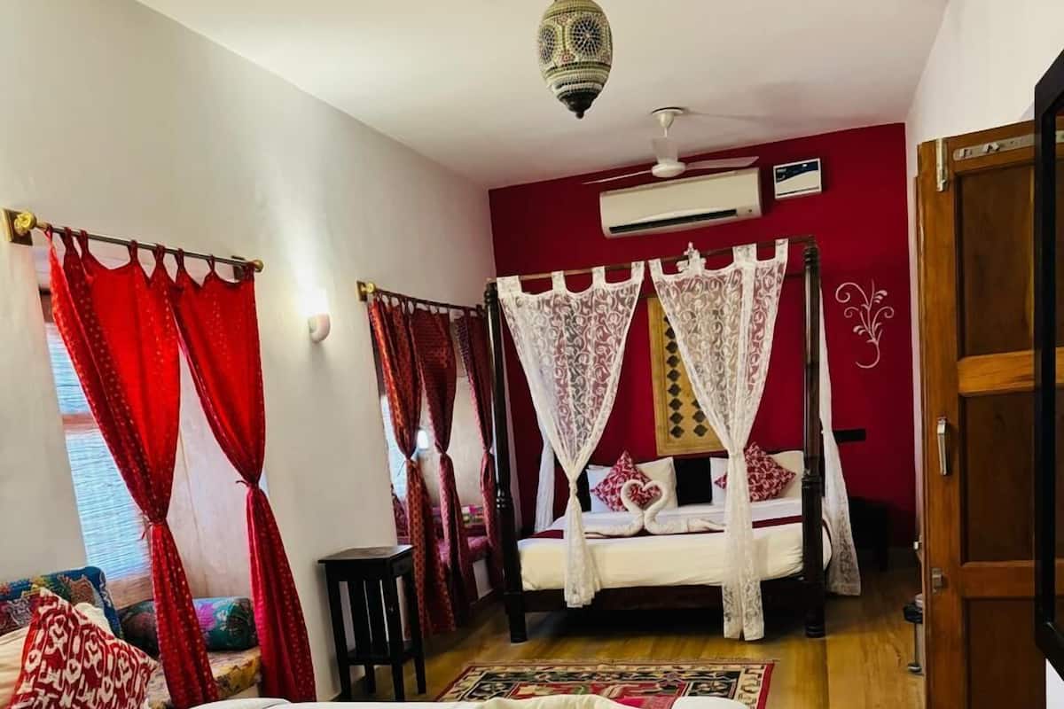 A room with a bed, a wooden floor, a red wall, a ceiling fan, and a decorative hanging light fixture.