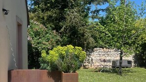 Un jardin avec un mur en pierre, un banc en bois et un bac en béton contenant des plantes.