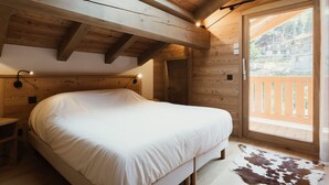 A wooden cabin bedroom with a bed, a nightstand, a skylight, and a view of a building through a glass door.