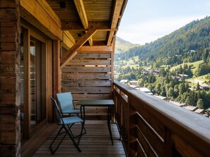 Een houten balkon met een tafel en stoelen, met uitzicht op een vallei met huizen en bomen.