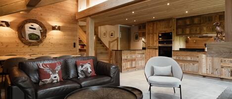 Un intérieur moderne avec un plafond en bois, un canapé en cuir agrémenté de coussins décoratifs, une table basse ronde et un fauteuil blanc.