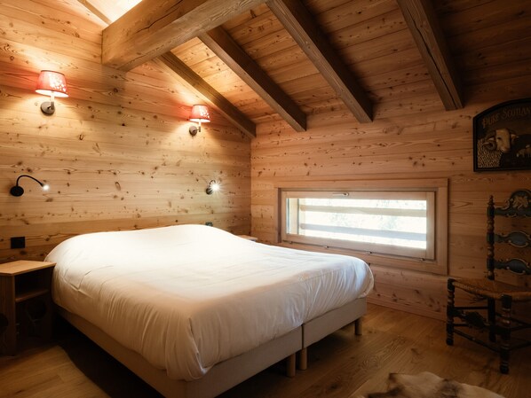 A wooden cabin bedroom with a bed, two wall-mounted lamps, a window, and a wooden headboard.