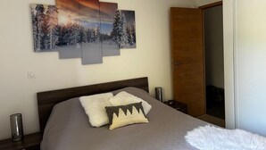 Een slaapkamer met een bed, nachtkastje, lamp en een deur.