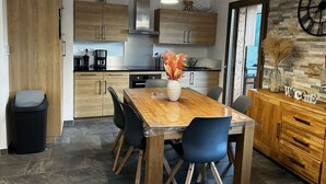 Een moderne keuken met houten kastjes, een eettafel met stoelen, een koffiezetapparaat en een klok aan de muur.