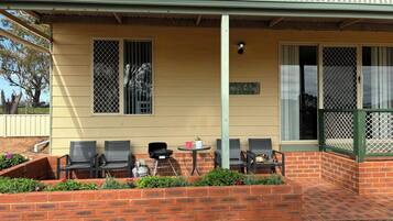 A covered outdoor seating area with brick walls, metal chairs, and a small table.
