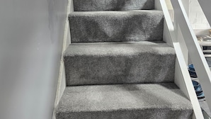 Un escalier dont les marches sont recouvertes de moquette et dont les rampes sont blanches.