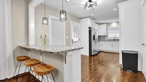A modern kitchen with a marble countertop, wooden stools, and pendant lighting. - Heart of Buckhead Message Now for Summer Special (Atlanta)