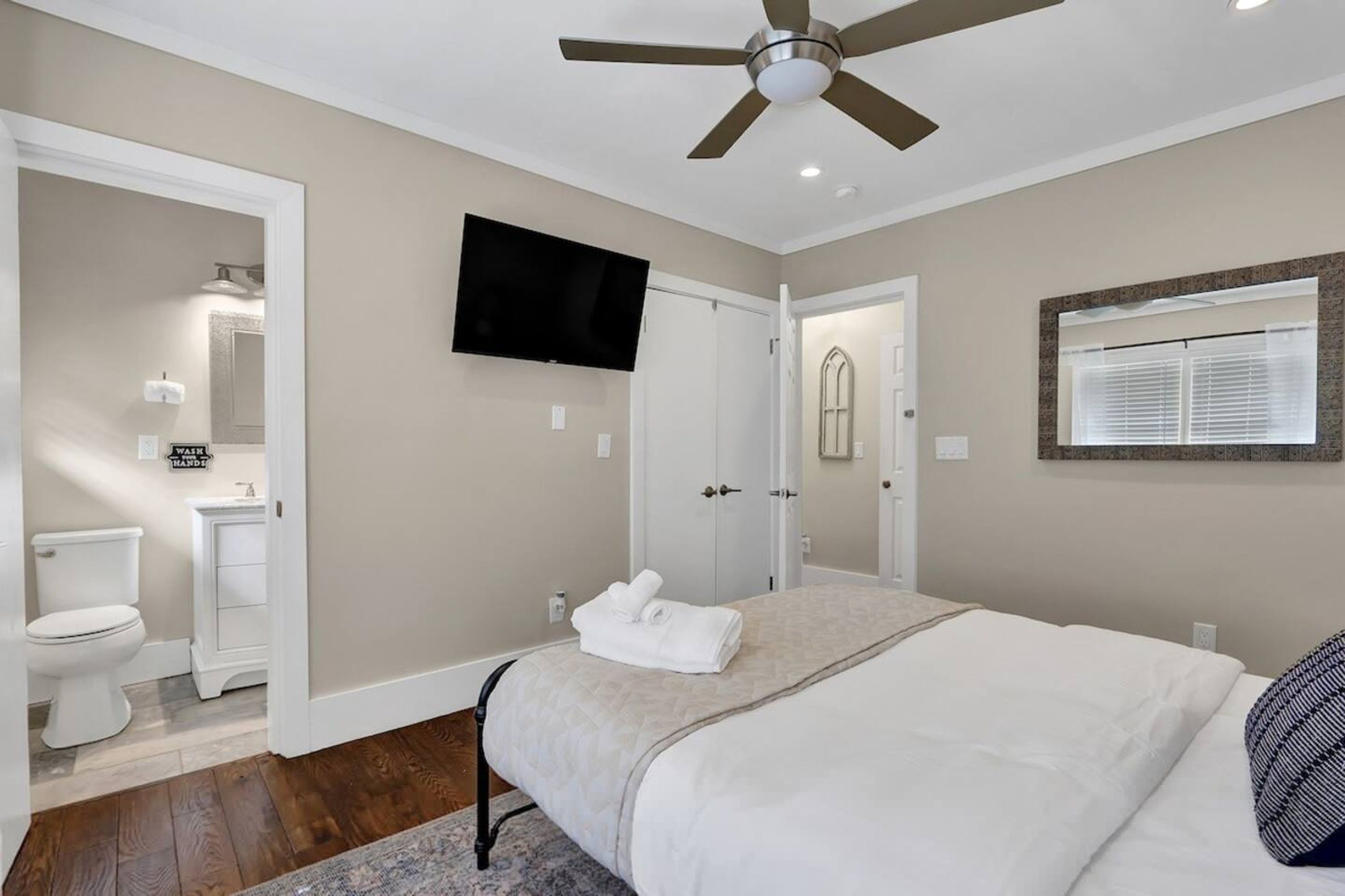 A bedroom with a bed, a ceiling fan, a TV, and a bathroom with a toilet and sink.