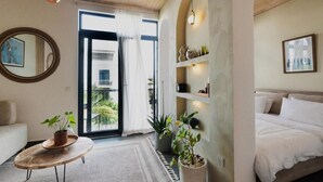 A modern bedroom with a bed, a small round table with a plant, a mirror, and a view of greenery outside. - Nafsi Nomad (Paje)
