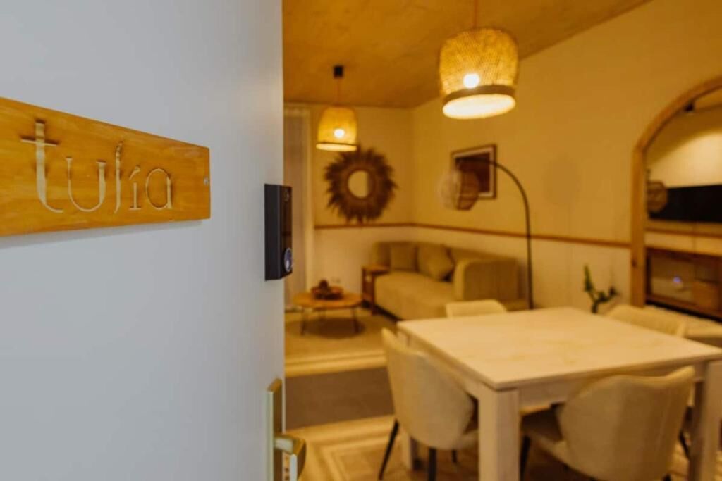 Een gezellige kamer met een houten bordje waarop 'tulia' staat, een eettafel met stoelen, een bank en een lamp.
